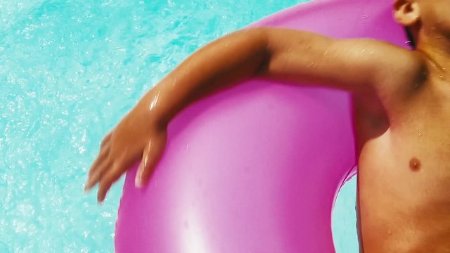 Extreme close up of little boy spinning in a purple tube in a bright swimming pool on a summer day.