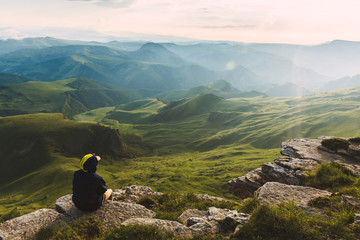 Travel man tourist sitting alone on the edge mountains over green valley adventure lifestyle extreme vacations green landscape Freedom - 276649448
