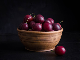 ripe plums in the bowl on black background