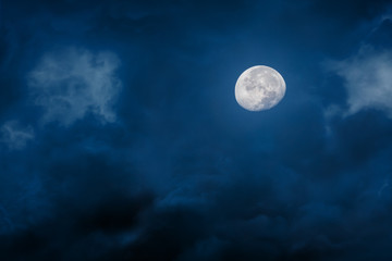 Moon at night with bright and dark clouds on blue background