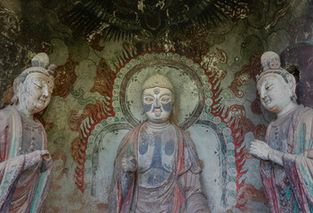 Sculpture of Buddha and two attendant Bodhisattva with colorful fresco in a niche of a grotto at Mount Maiji or Maijishan Grottoes, Tianshui, Gansu, China. Constructed from late fourth century CE.