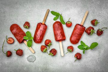 Natural juicy strawberry popsicle. Red frozen sorbet with blended fruits. Red popsicles, flat lay.