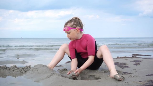 Slow-motion video of pretty girl in neoprene swimsuits running on the beach and playing with waves and sand