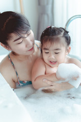 Young asian mother and daughter in a bathroom happy smiling taking bath