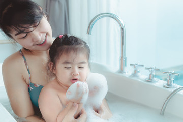 Young asian mother and daughter in a bathroom happy smiling taking bath