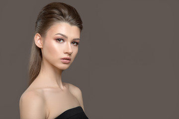 beautiful young woman over gray background. Nude, bare shoulders. Perfect skin and hair styling