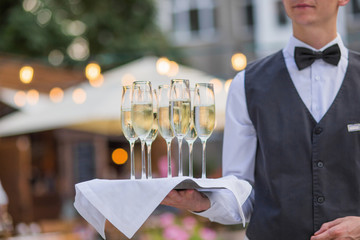 Catering service waiter holding a tray with glasses of Italian and French wine prosecco and...
