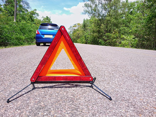 Emergency red warning triangle on the road sign with a blue broken car