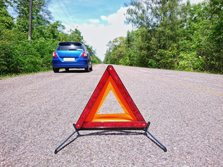 Emergency red warning triangle on the road sign with a blue broken car