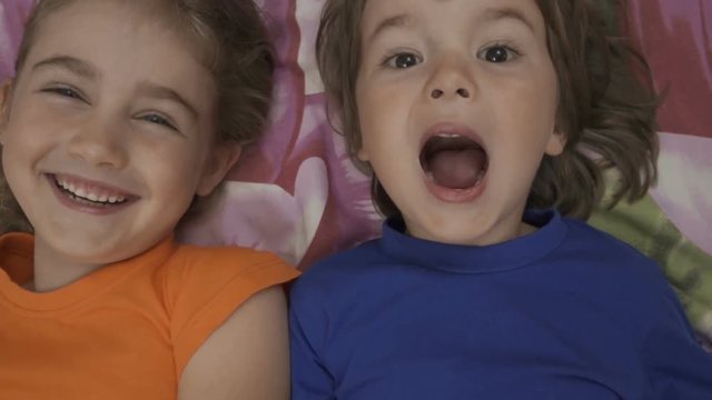 Family selfie. Excited young children playing lying on the bed and taking a selfie. Little brother and sister monkeying on camera and kissing.  Family taking a selfie with a smartphone. Close up.