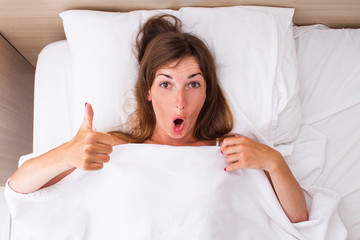 A young woman with a surprised face is lying in bed. Concept insomnia, dreams, sleeping pills, good...