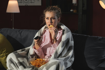 Beautiful young woman eating unhealthy food while watching TV at night