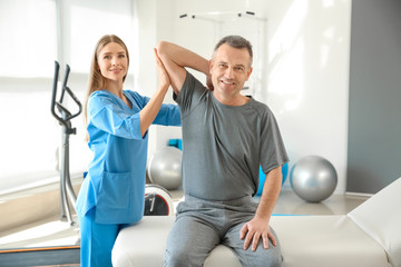 Physiotherapist working with mature patient in rehabilitation center - obrazy, fototapety, plakaty