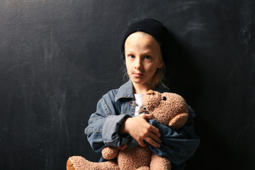 Homeless little girl with teddy bear on dark background