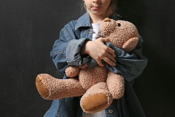 Homeless little girl with teddy bear on dark background
