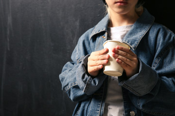 Homeless little girl with cup on dark background