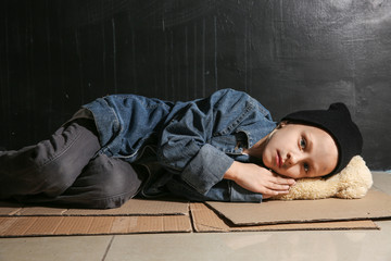 Homeless little girl lying on floor near dark wall