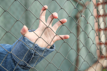 Hand of homeless little girl behind mesh outdoors