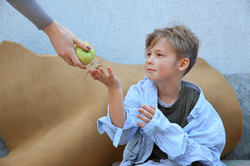 Woman giving food to homeless little boy outdoors