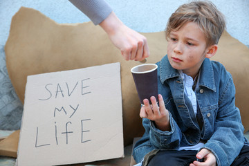 Woman giving money to homeless little boy outdoors