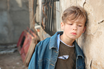 Homeless little boy near wall outdoors