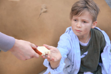 Woman giving food to homeless little boy outdoors