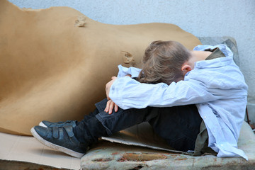 Homeless little boy sitting outdoors