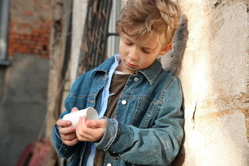 Homeless little boy counting money outdoors