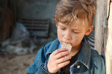 Homeless little boy eating bread outdoors