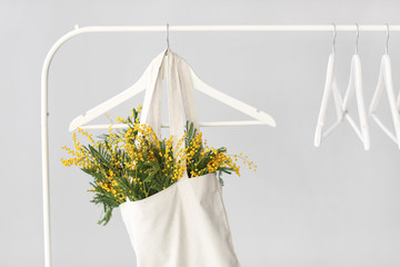 Bag with bouquet of mimosa flowers hanging on rack against light background