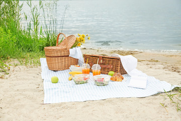 Wicker baskets with tasty food and drink for romantic picnic near river - obrazy, fototapety, plakaty