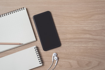 Workspace with diary or notebook and smart phone, Earphone, pencil on wooden background