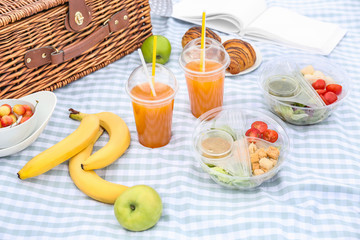 Wicker basket with tasty food and drink for romantic picnic on plaid