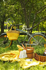 Bicycle and wicker baskets with tasty food and drink for romantic picnic in park