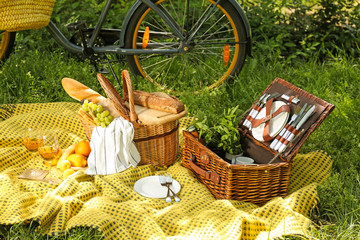 Wicker baskets with tasty food and drink for romantic picnic in park - obrazy, fototapety, plakaty