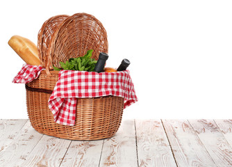 Wicker basket with tasty food and drink for picnic on wooden table against white background