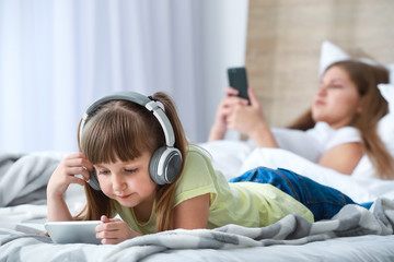 Little girl with addiction to modern technologies lying with mobile phone on bed at home