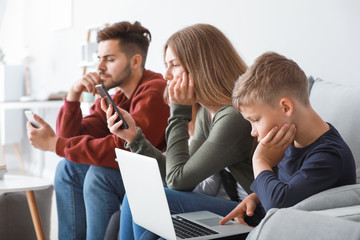 Family addicted to modern technologies with devices sitting on sofa at home