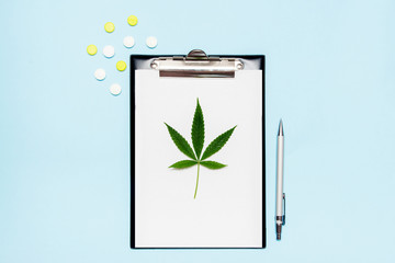 Top view of blank paper for writing doctor prescription. Marijuana leaf with medical pills on blue background. The concept of legalization of marijuana.