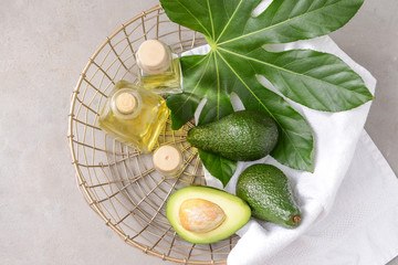 Basket with fresh ripe avocados and essential oil on grey table