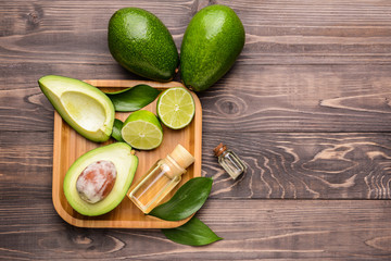 Plate with fresh ripe avocados, lime and essential oil on wooden table
