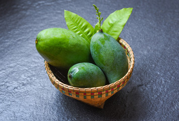 Green Mango summer fruit and green leaves in the basket on dark background - Fresh raw mango