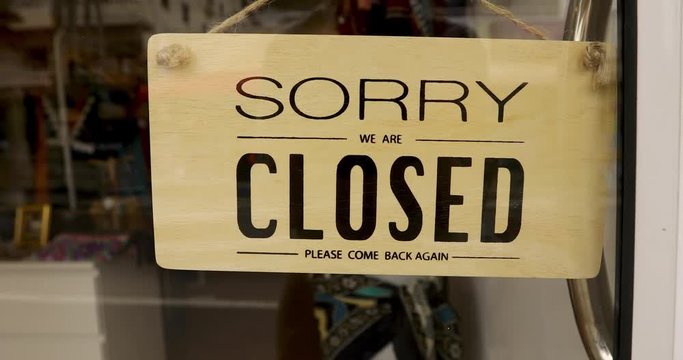 Inscription Sorry closed on wooden banner hanging on glass door in shop