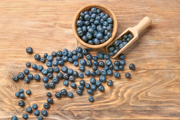 Bowl and scoop with ripe blueberry on wooden background