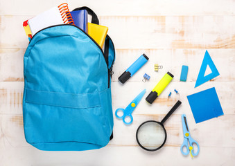 School backpack and stationery on light wooden background