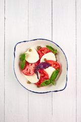 caprese salad at white wooden table top. italian cuisine appetizer with tomato, mozzarella, basil and olive oil or pesto sauce. vegetarian dish .top view.  vertical