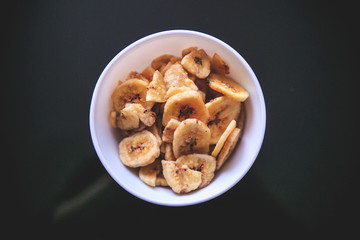 Dried bananas in the white bowl on the black background taken from the top.