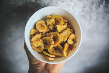 Dried bananas in the white bowl on the gray and white background taken from the top. © alexis