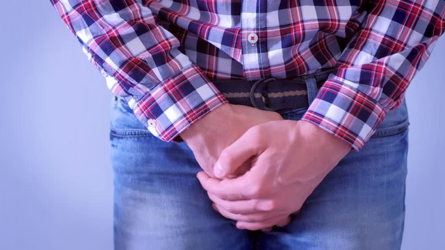 Man wants to pee and feels pain, grabbing himself on crotch in jeans by hands. Sexual transmitted diseases concept.