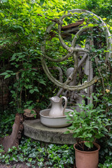 überwuchertes Brunnenrad in einem Garten mit Keramikgefäßen